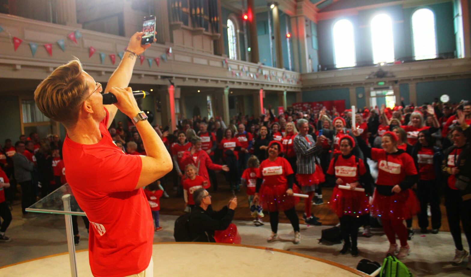 Rod Buchanan stands on stage holding a mic and leading a crowd of people in a warmup before The Twilight Walk
