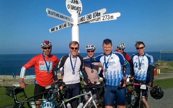 A supporter group associated with The Brain Tumour Charity stands with bicycles in front of a road sign at John o' Groats