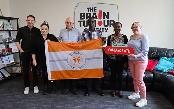People from a trust hold a flag with members of The Brain Tumour Charity in The Charity's office