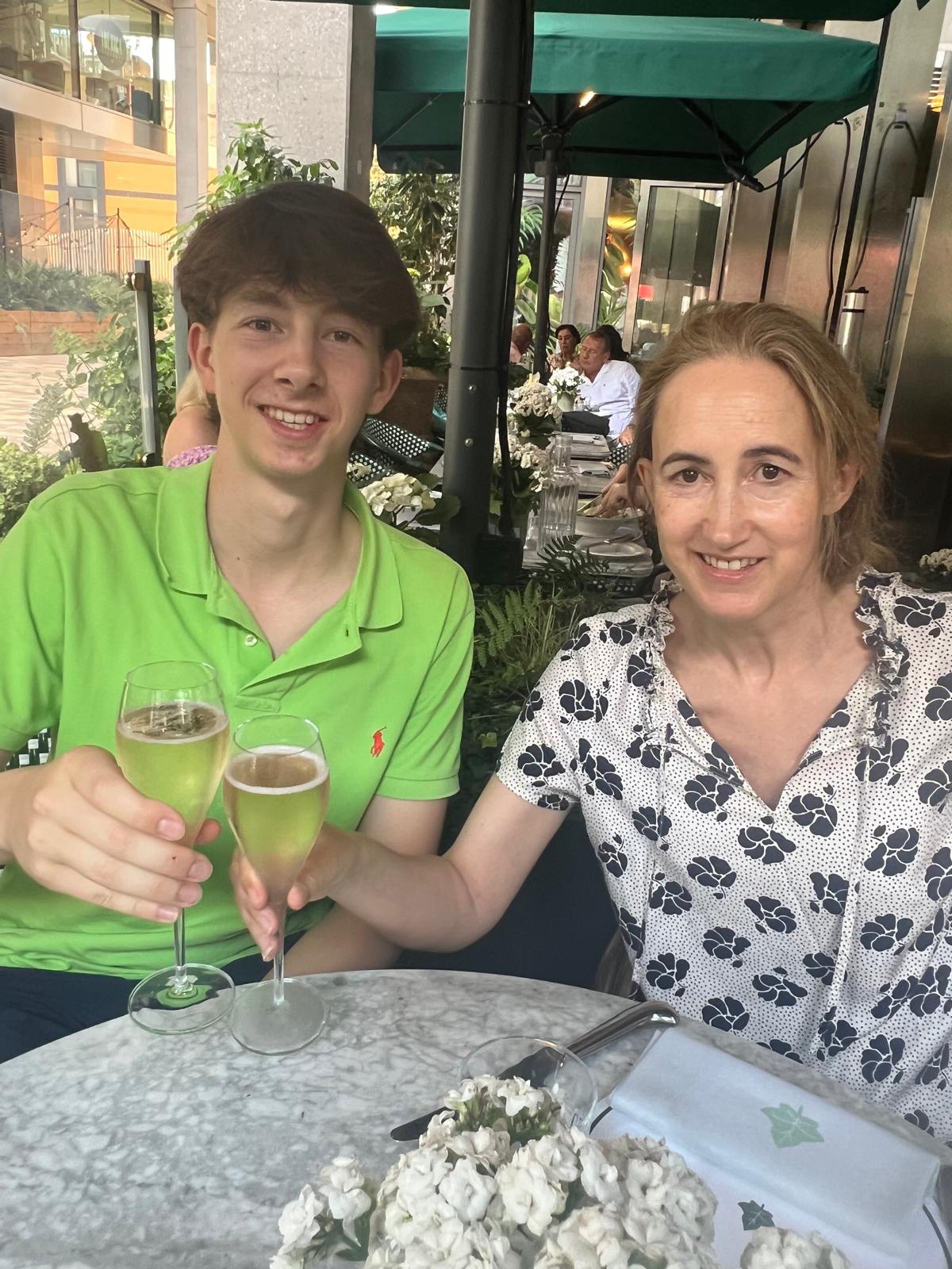 Sophie Kinsella and her son Oscar holding up wine glasses in the outdoor section of a restaurant
