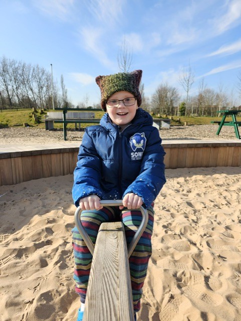A young child, Ezra, on a seesaw in a playground