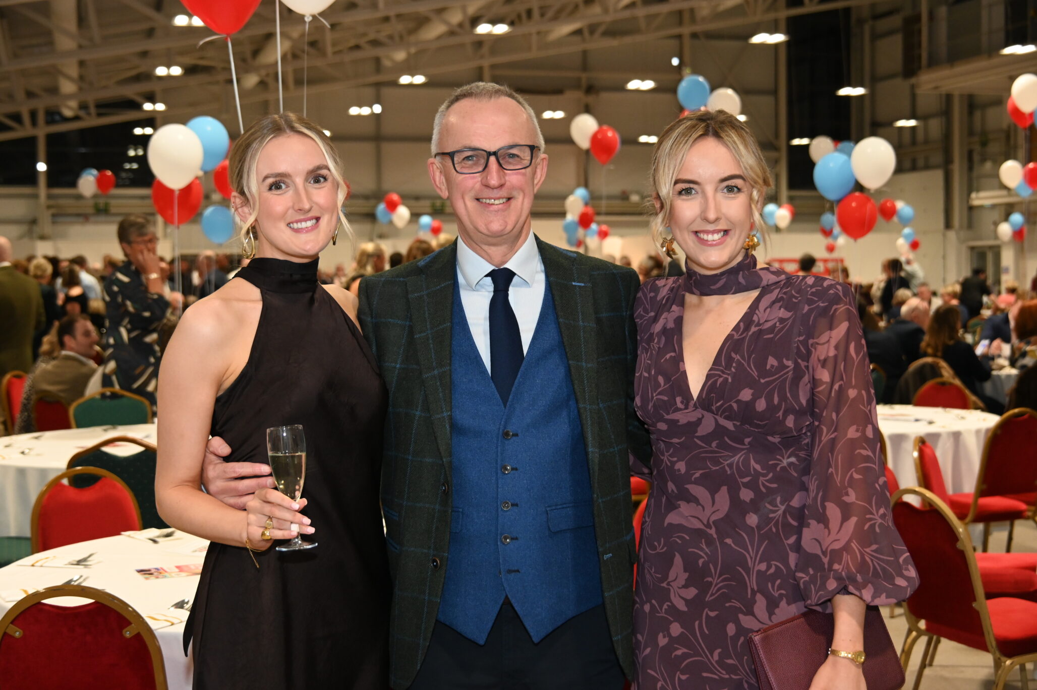 Gareth Davies and daughters, Gwen and Elin stand at a gala dinner with red, white, and teal balloons in the background. They are among The Brain Tumour Charity's London Marathon 2026 runners
