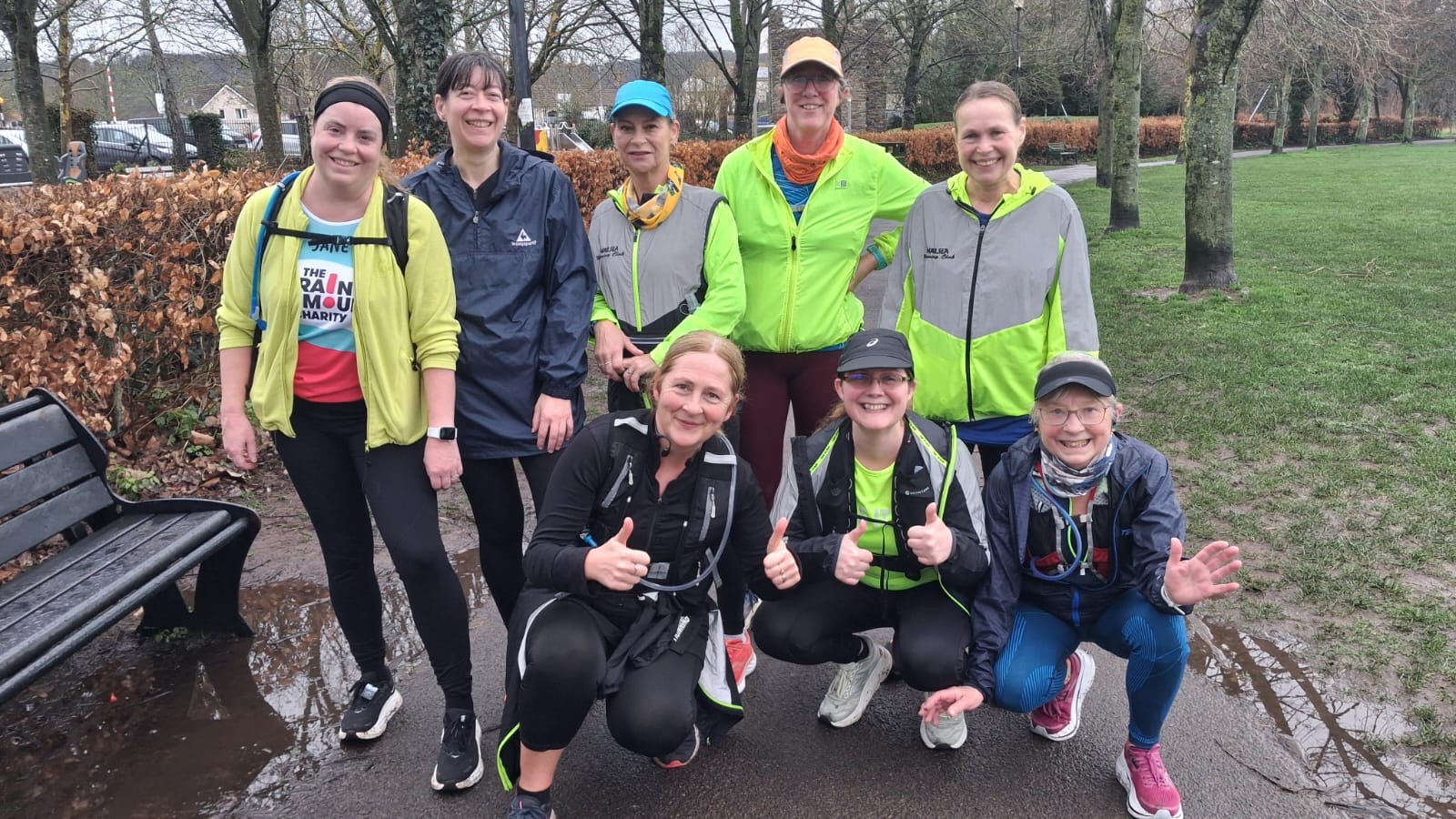 A group of friends stand in high vis running wear in a wet park on a rainy day