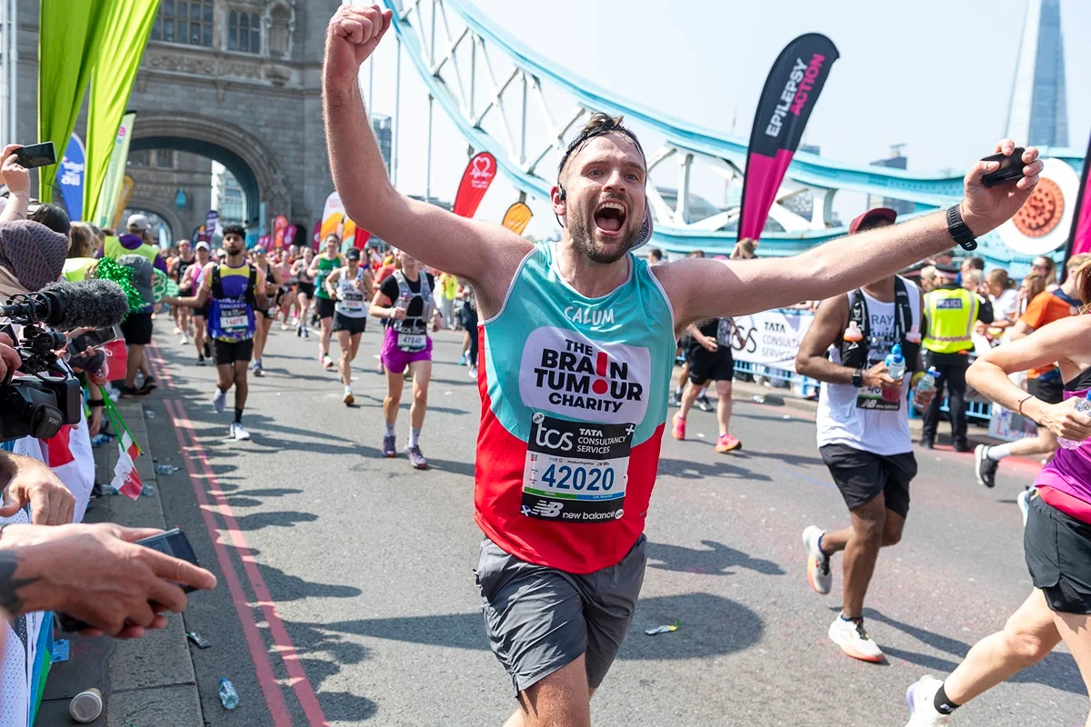 Calum Lazenby holds his arms up while running across Tower Bridge during the London Marathon 2025 