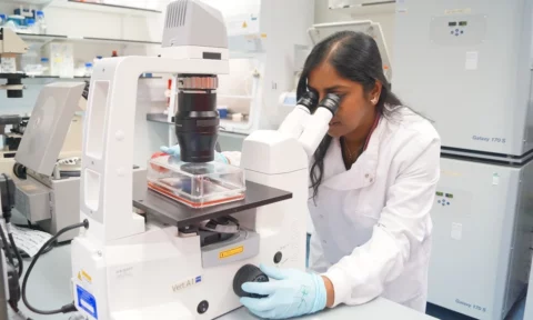 Researcher in a white lab coat looking into a microscope