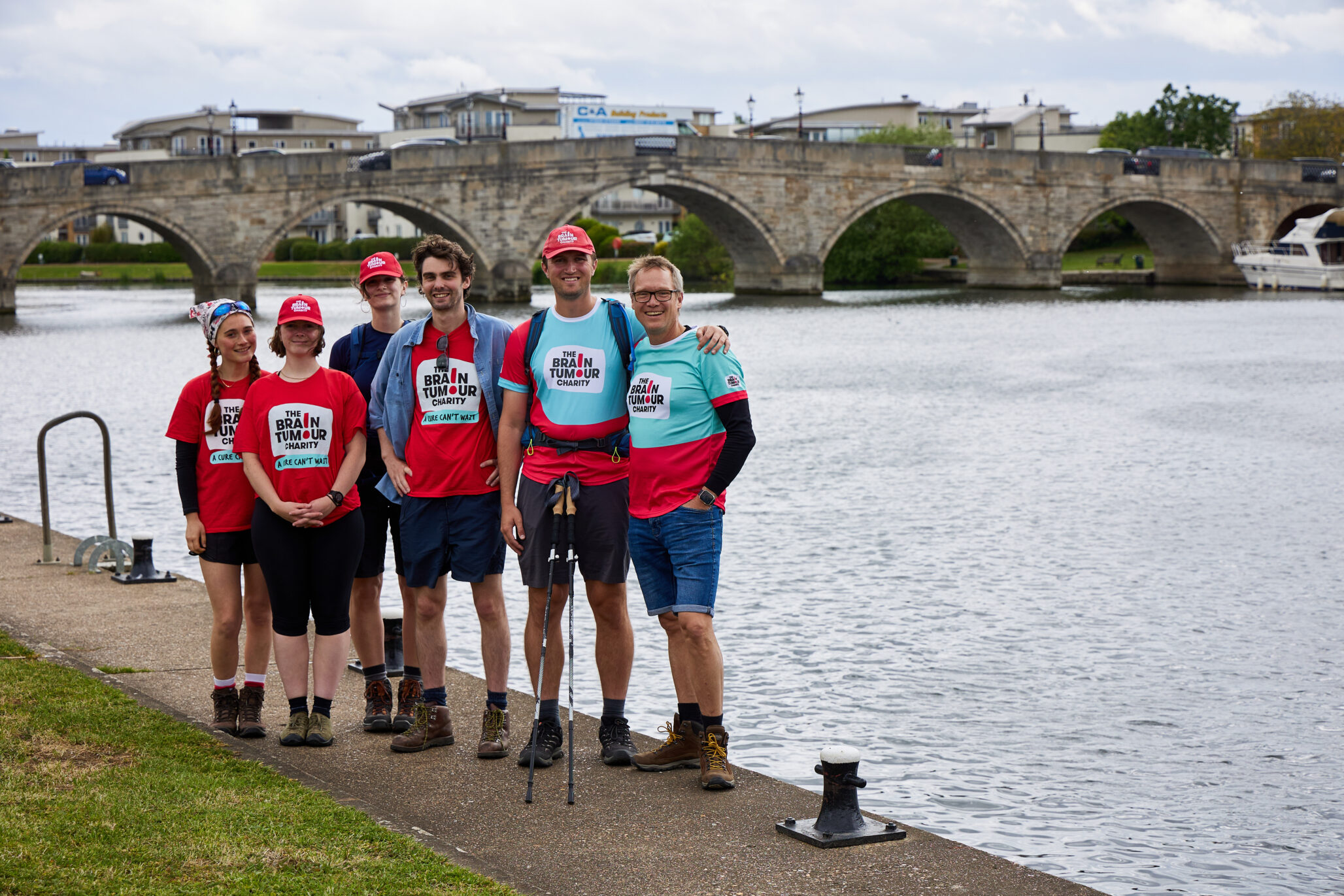 A group of walkers for The Brain Tumour Charity stand with a Thames bridge in the background during their Thames Path Walk challenge