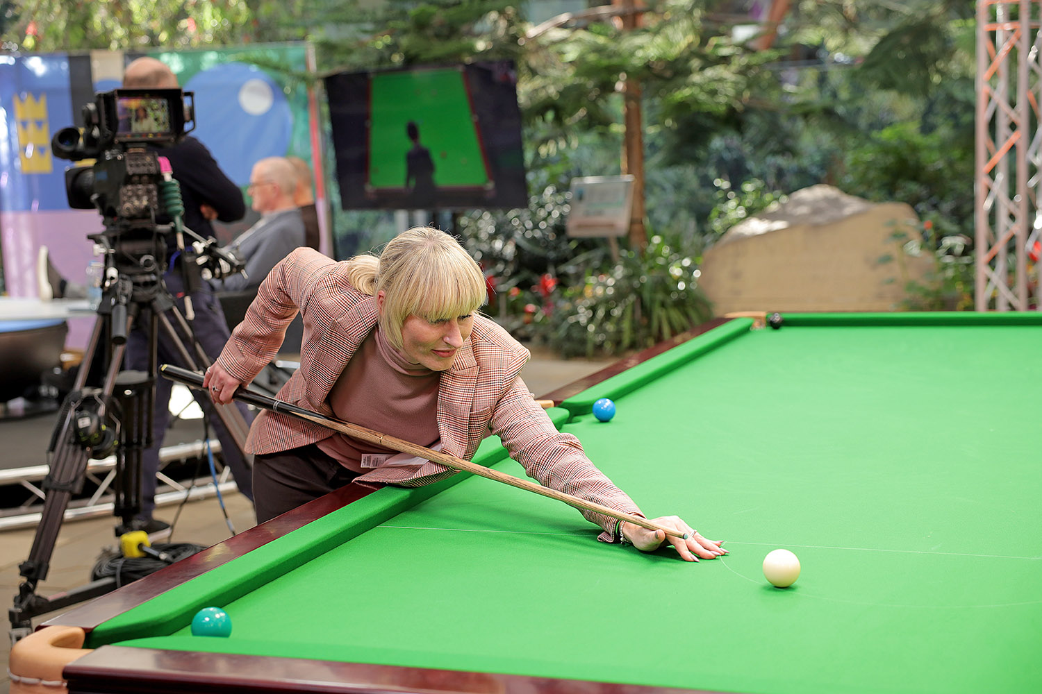 A woman lines up a shot on a snooker table with a film camera behind her