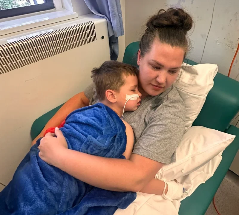 Reggie's mum holds him while he sleeps. He has a bandage on his face holding his oxygen tube in place.