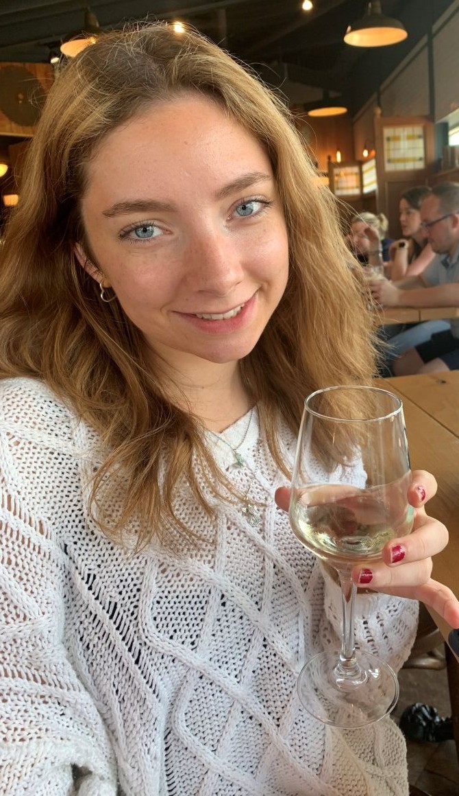 Annie who has long fair hair and is wearing a white top, holding a drink
