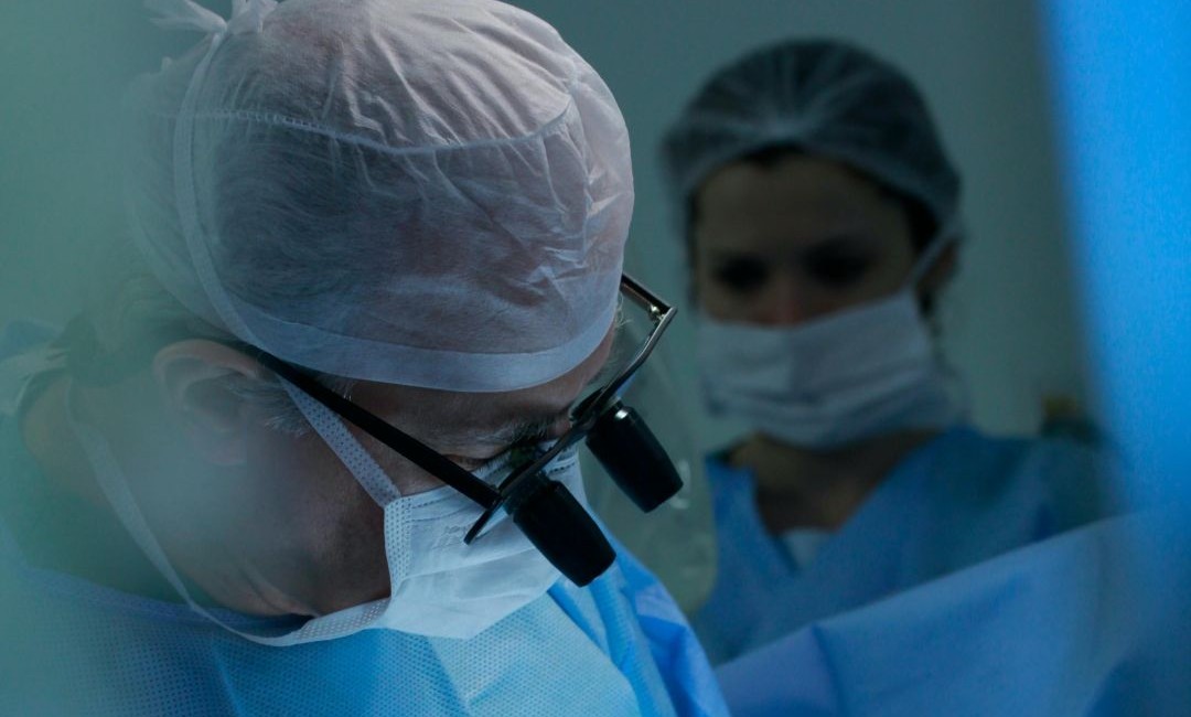A surgeon with magnifying glasses and a face mask performs a surgery. This will be safer for brain tumours as a result of the Cancer Tech Accelerator.
