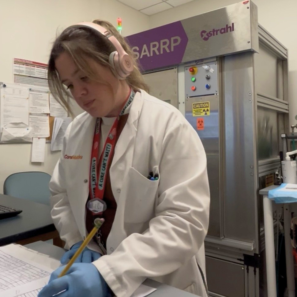 Mara De Martino working in the lab, wearing a white lab coat and a The Brain Tumour Charity lanyard