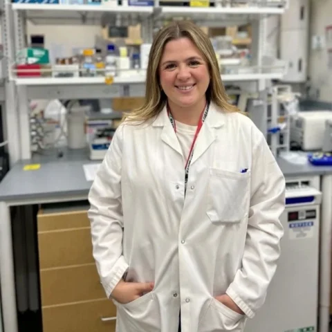 Dr Mara De Martino stands in a lab wearing a white lab coat