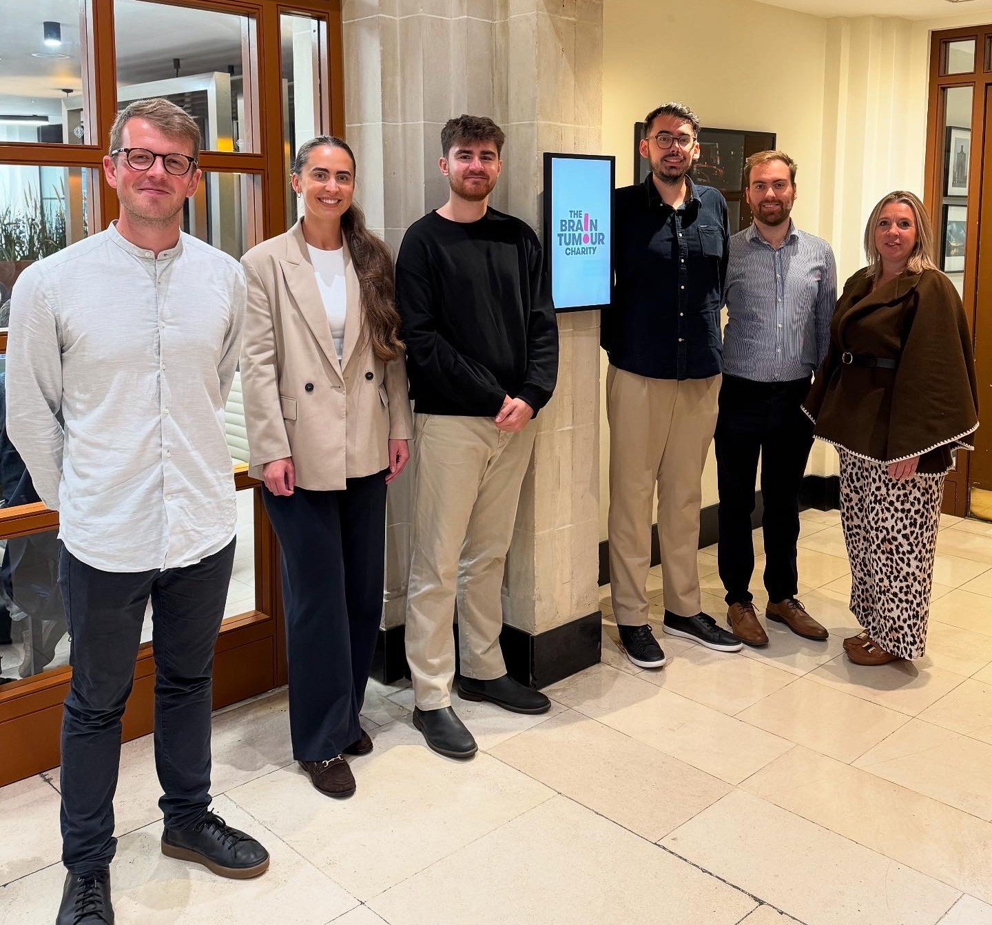 Hannah in cream jacket next to Owen Sutton in black jumper and The Brain Tumour Charity team.