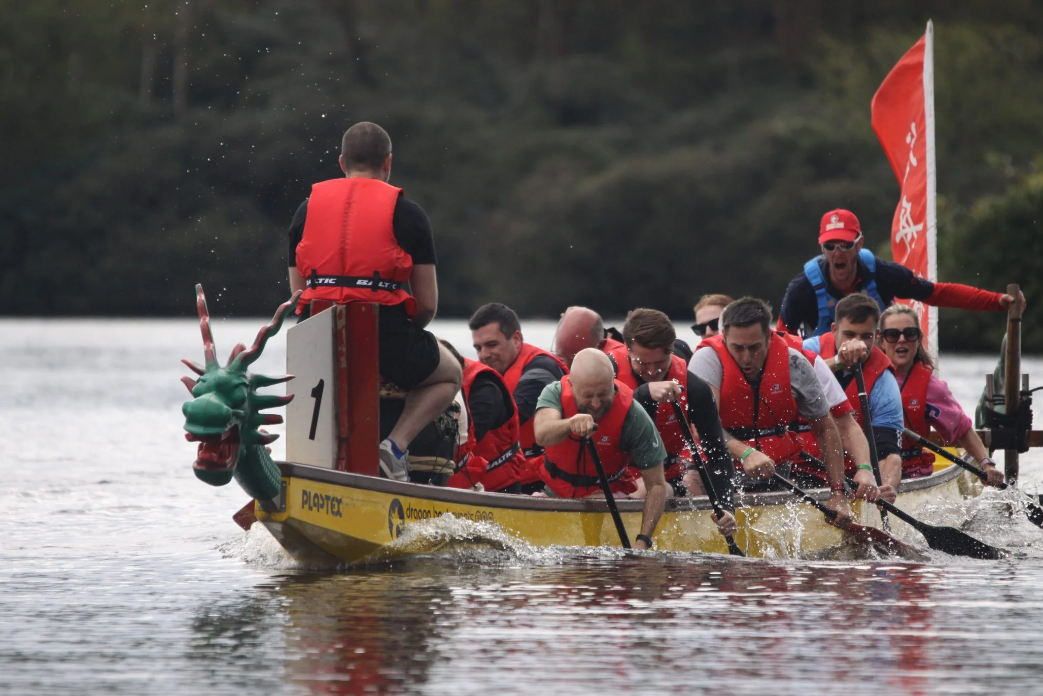 A group of people in a Dragon Boat, rowing on a still lake